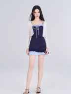 Full-length view of a model in a navy blue one-piece swimsuit with light blue gingham trim and a white sheer cardigan.