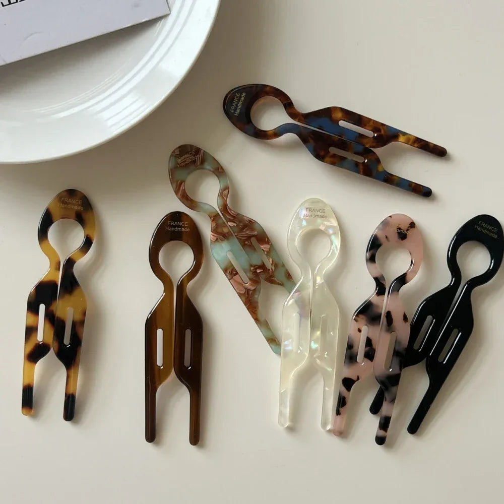 Multiple resin tweezers in different patterns and colors, including tortoise shell, marbled, and solid black, laid out on a white surface.