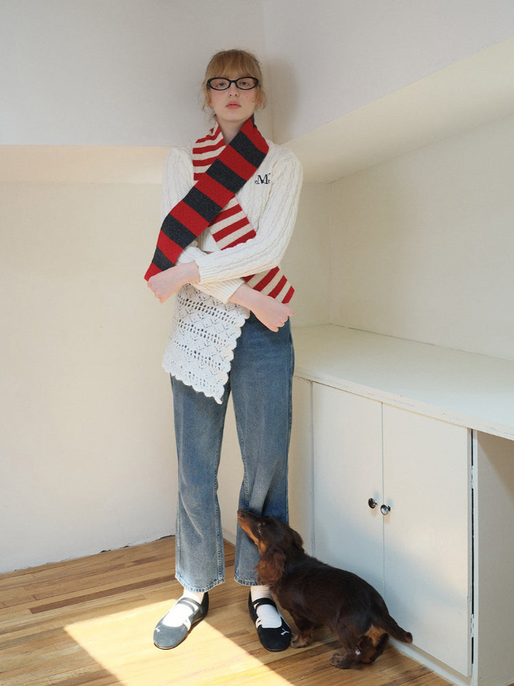 Model wearing a white sweater, blue jeans, and a red, grey, and white striped scarf, with a small dog.