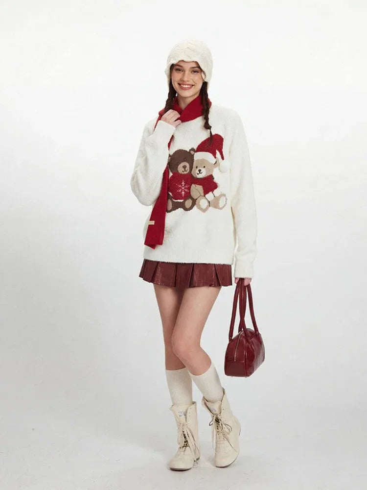Model wearing a white fuzzy knit sweater with a graphic of two teddy bears, a red scarf, white beanie, red pleated skirt, white socks, and cream boots. Secondary image
