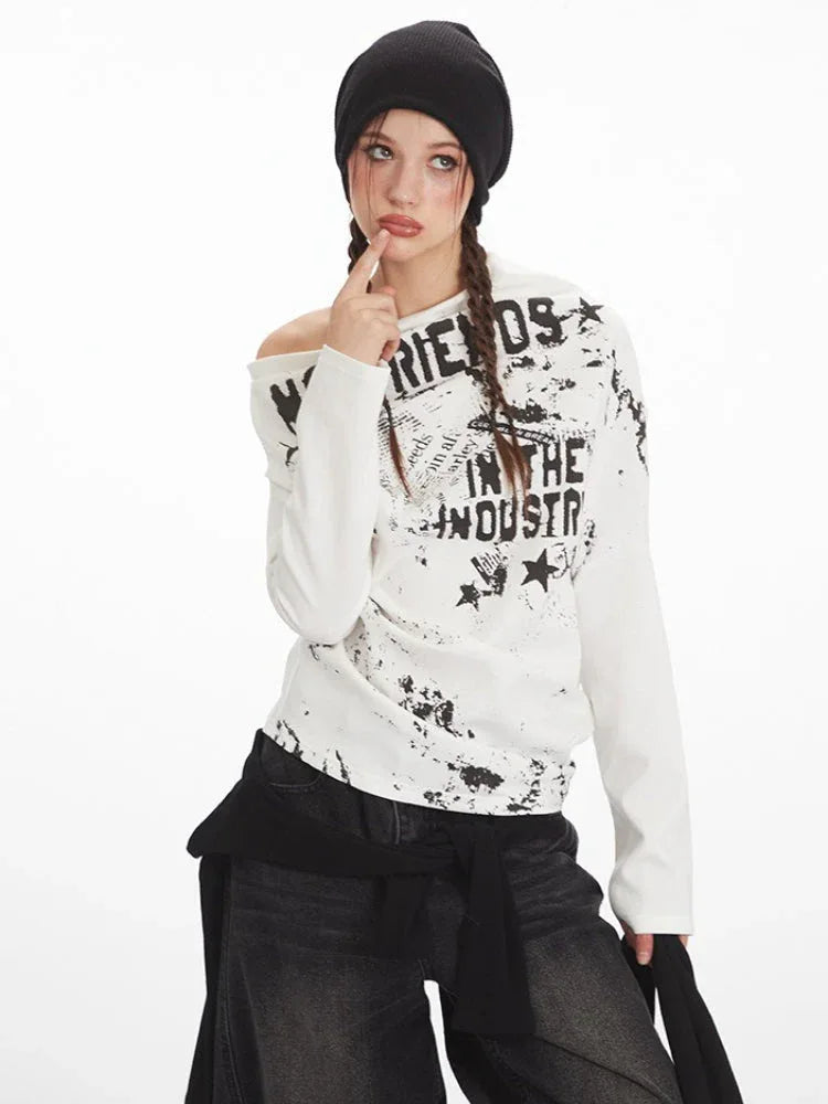 Close-up of a model wearing a white long-sleeved off-the-shoulder top with distressed graphic print, showing facial details.