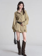 A model showcases a tan shirt dress with a gathered skirt, black studded belt, grey socks, and dark brown boots.