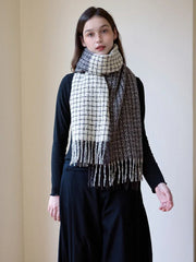 Woman wearing a black long-sleeve top and a plaid scarf with fringe detail, styled loosely around her neck.