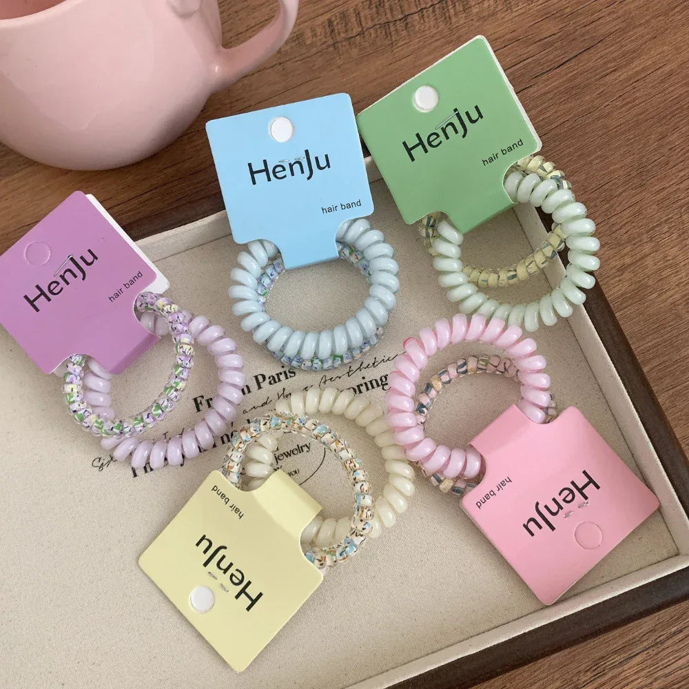 A collection of pastel-colored spiral hair ties with beaded accents, displayed on a tray.