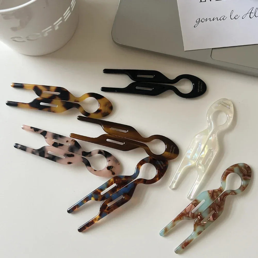 Assortment of resin tweezers in various patterns (tortoise shell, marbled, solid colors) arranged on a white surface next to a laptop and coffee cup.