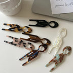 Assortment of resin tweezers in various patterns (tortoise shell, marbled, solid colors) arranged on a white surface next to a laptop and coffee cup.