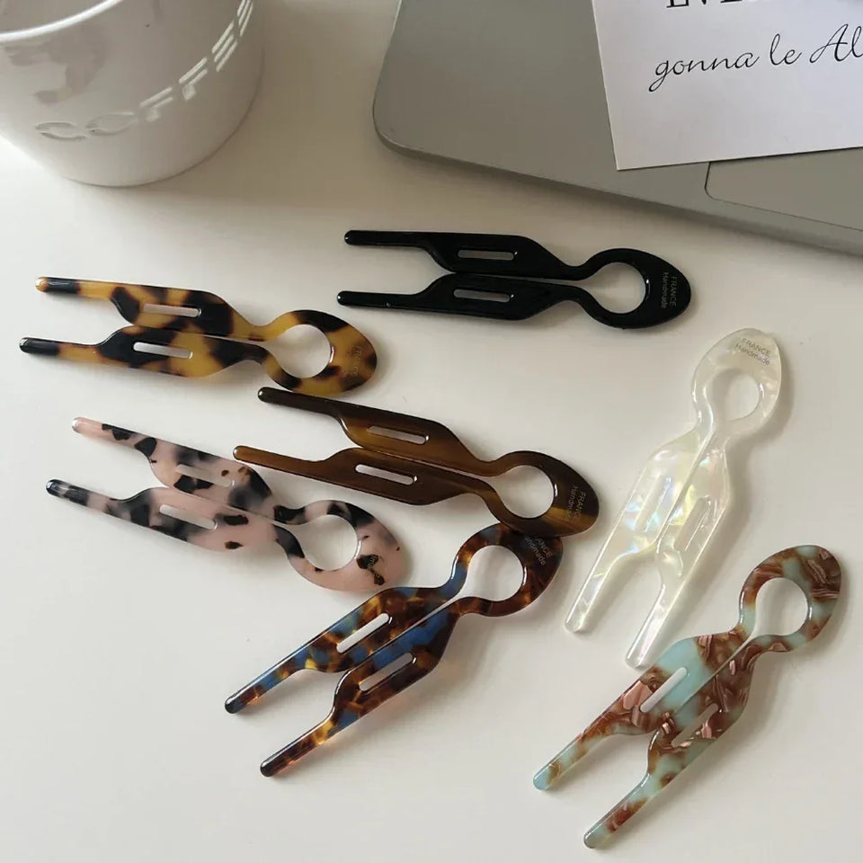 Assortment of resin tweezers in various patterns (tortoise shell, marbled, solid colors) arranged on a white surface next to a laptop and coffee cup. Secondary image