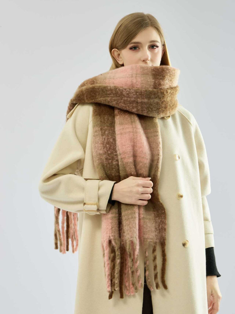 Close-up of a woman adjusting a large plaid scarf in pink and brown tones.