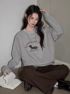 Woman sitting and reading a book, wearing a grey crew neck sweatshirt with a dachshund graphic and text "SUNLIGHT DAY".