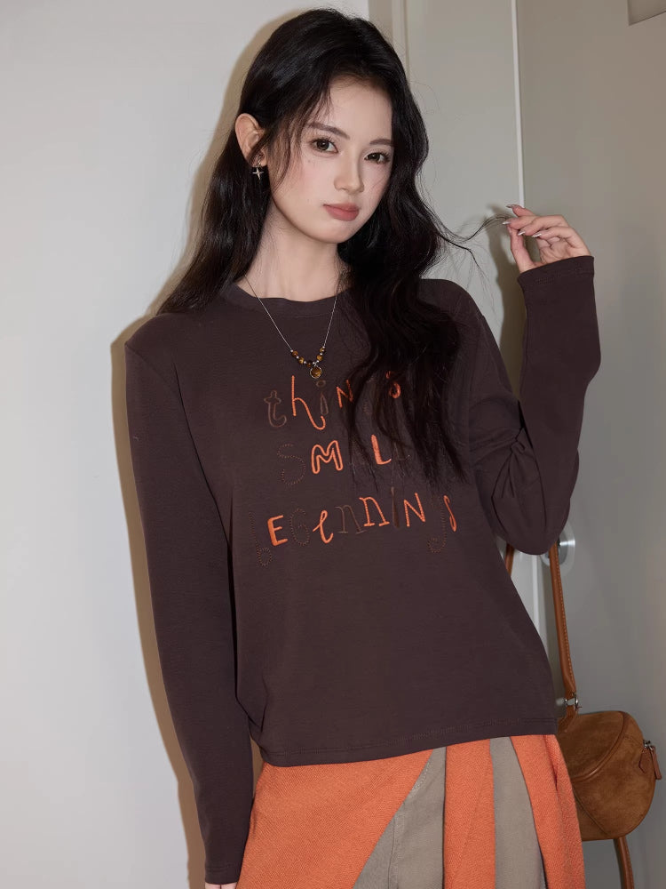 Close-up of a young woman wearing a brown long-sleeved graphic t-shirt