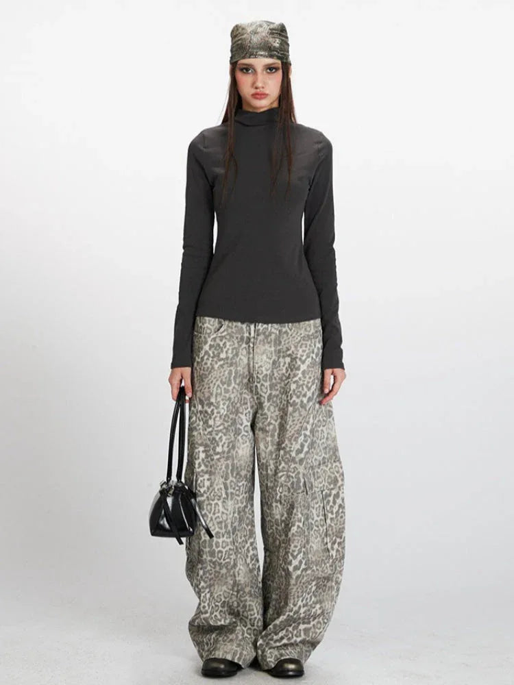Woman wearing a dark grey long-sleeved turtleneck top with a leopard print wide-leg cargo pants and a patterned headscarf, holding a black handbag.