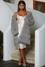 Woman wearing a gray faux fur coat draped over a cream slip dress, standing on a curved staircase.