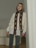 Model leaning against a wall wearing a cream sweatshirt and argyle scarf