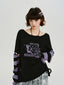 Model wearing a black knit sweater with purple graphic print and striped sleeves