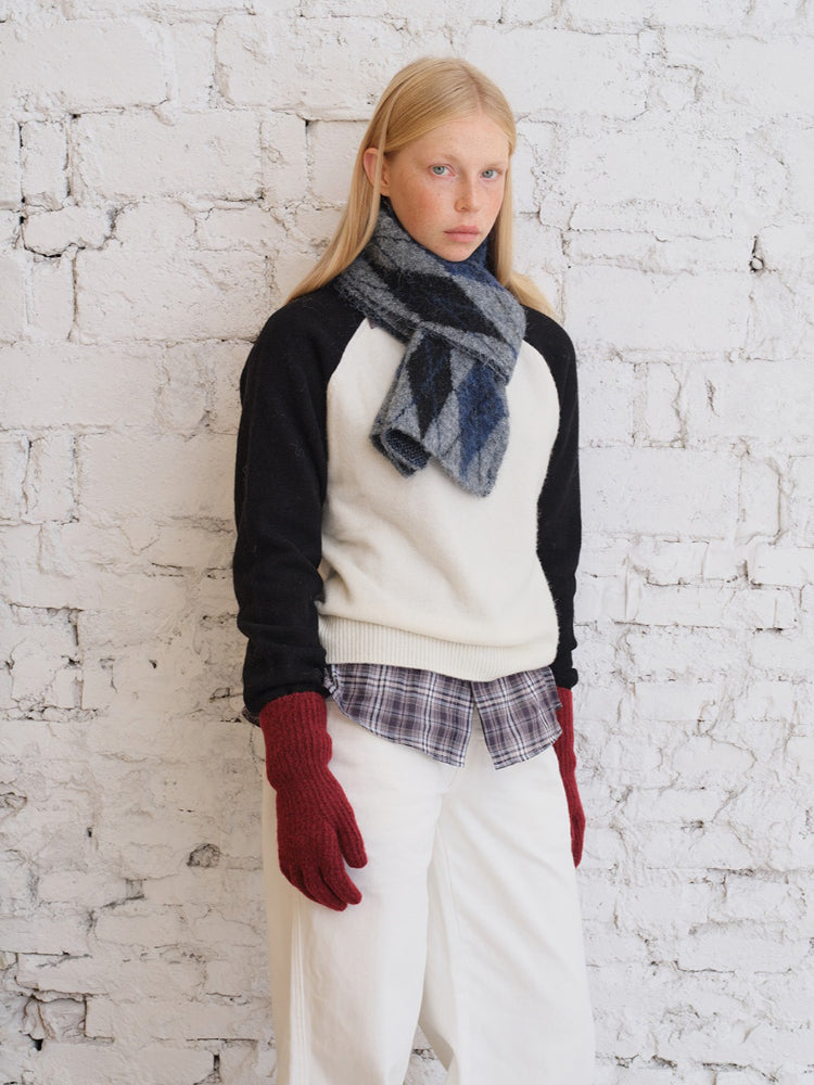 Model wearing a cream and black sweater with a striped scarf and white pants