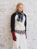 Model wearing a cream and black sweater with a striped scarf and white pants