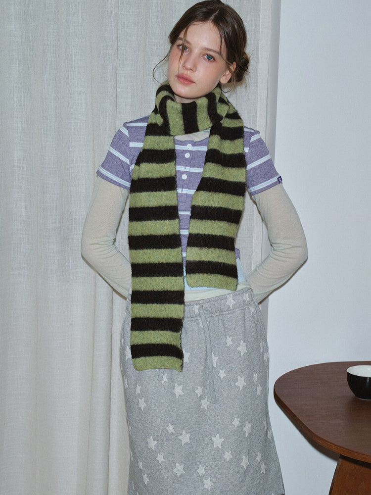 Woman wearing a striped scarf over a purple striped shirt and grey sweatpants with stars, posing with her hand on her hip.