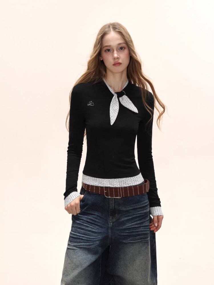 Model wearing a black long-sleeve top with a white polka dot scarf detail and white polka dot cuffs, paired with denim jeans and a brown belt.