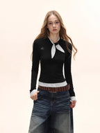 Model wearing a black long-sleeve top with a white polka dot scarf detail and white polka dot cuffs, paired with denim jeans and a brown belt.