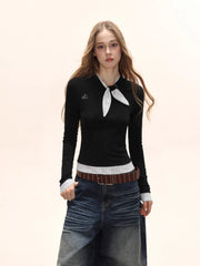 Model wearing a black long-sleeve top with a white polka dot scarf detail and white polka dot cuffs, paired with denim jeans and a brown belt.
