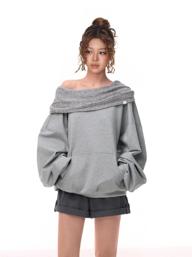 Front view of a model in a grey off-the-shoulder sweatshirt with a ribbed neckline and voluminous sleeves, hands in pockets.