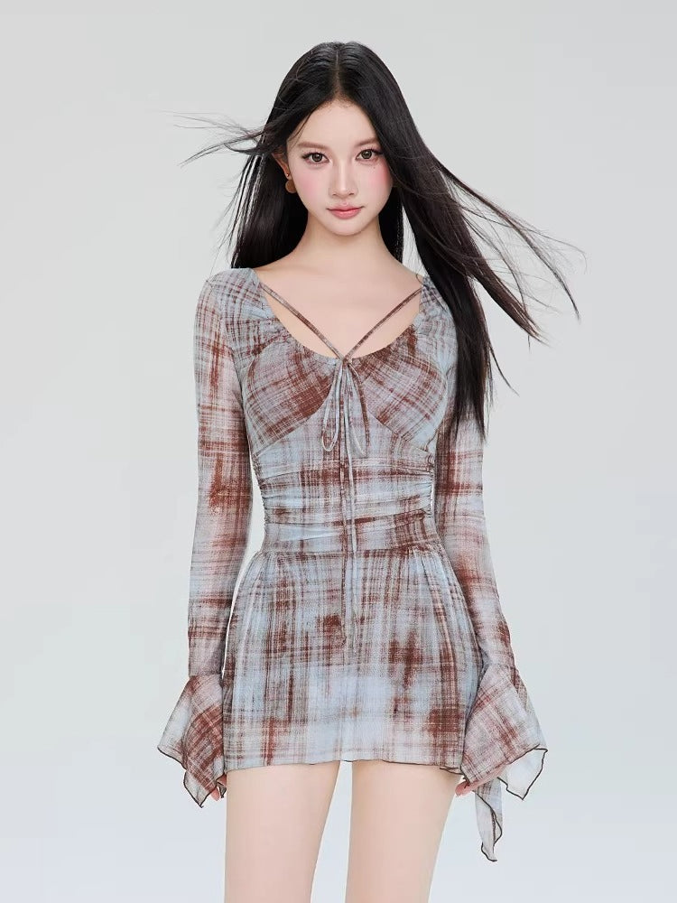 Woman wearing a long-sleeved, plaid mesh mini dress with a tie-front detail and flared sleeves.