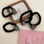 Three black velvet scrunchies with square leopard print pendants arranged on a wooden tray and a pink book
