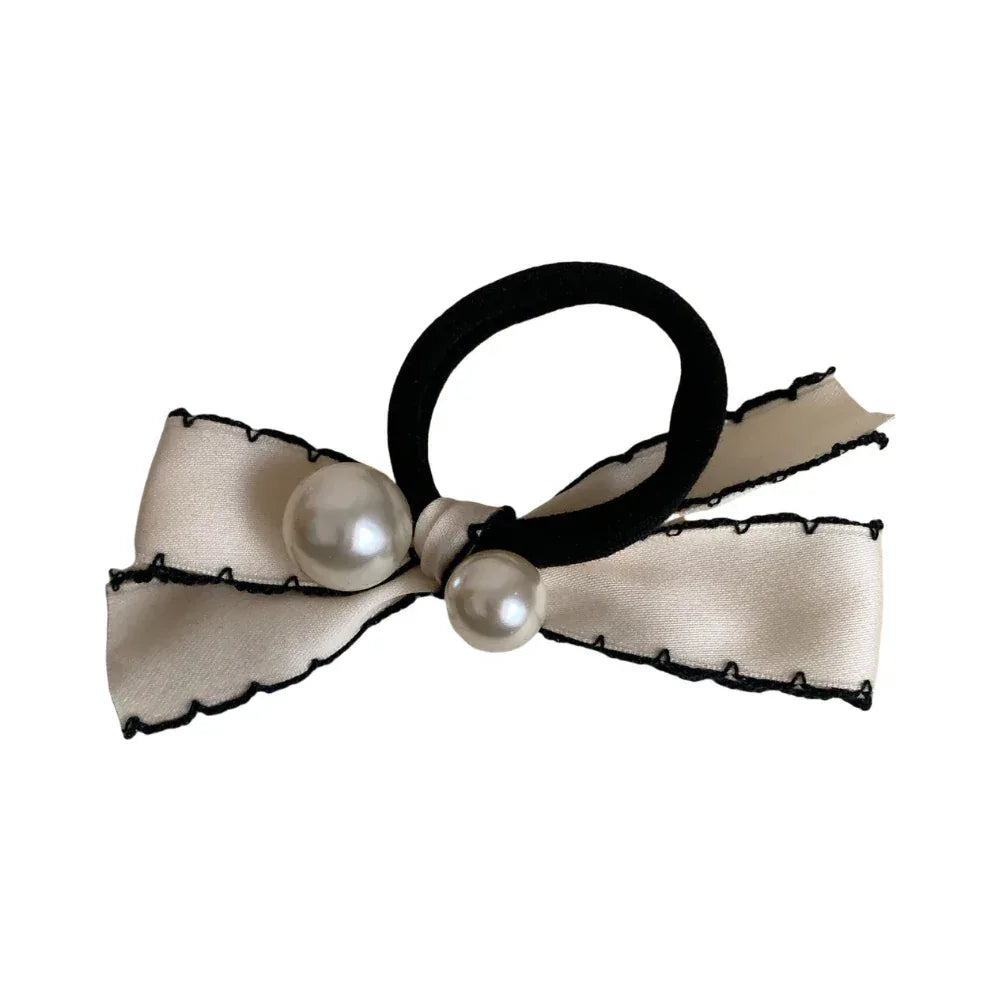 A close-up shot of a cream-colored bow hair tie with black trim and two pearls. Main image