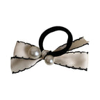 A close-up shot of a cream-colored bow hair tie with black trim and two pearls.