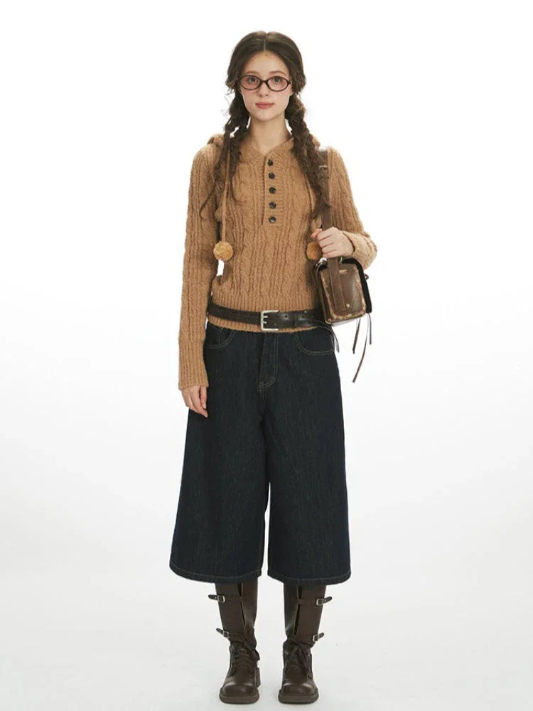 Woman wearing a brown cable knit hooded sweater with buttons and pom-poms, dark wash wide-leg cropped jeans, a black belt, brown boots, and a small brown crossbody bag.