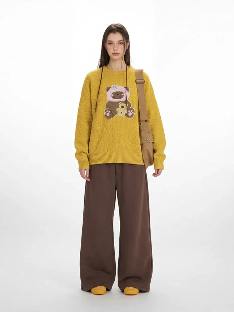 Woman wearing a yellow crew neck sweater with a bear graphic and brown wide-leg pants, with a brown crossbody bag. Main image