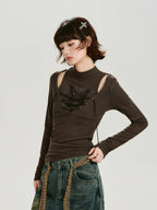 Side view of a model in a brown long-sleeved ribbed top with cut-out shoulders and lace-up detail, paired with distressed jeans.