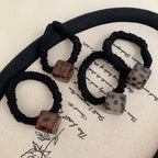 Set of four black velvet scrunchies with square leopard print pendants in various brown and grey tones