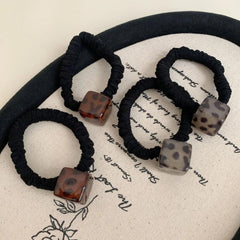 Set of four black velvet scrunchies with square leopard print pendants in various brown and grey tones