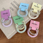 Assorted pastel spiral hair ties with beaded details, arranged on a book and wooden surface.