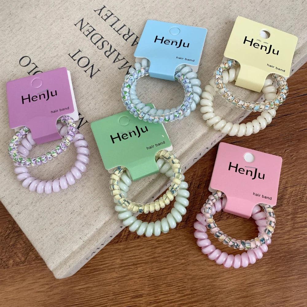 Assorted pastel spiral hair ties with beaded details, arranged on a book and wooden surface.