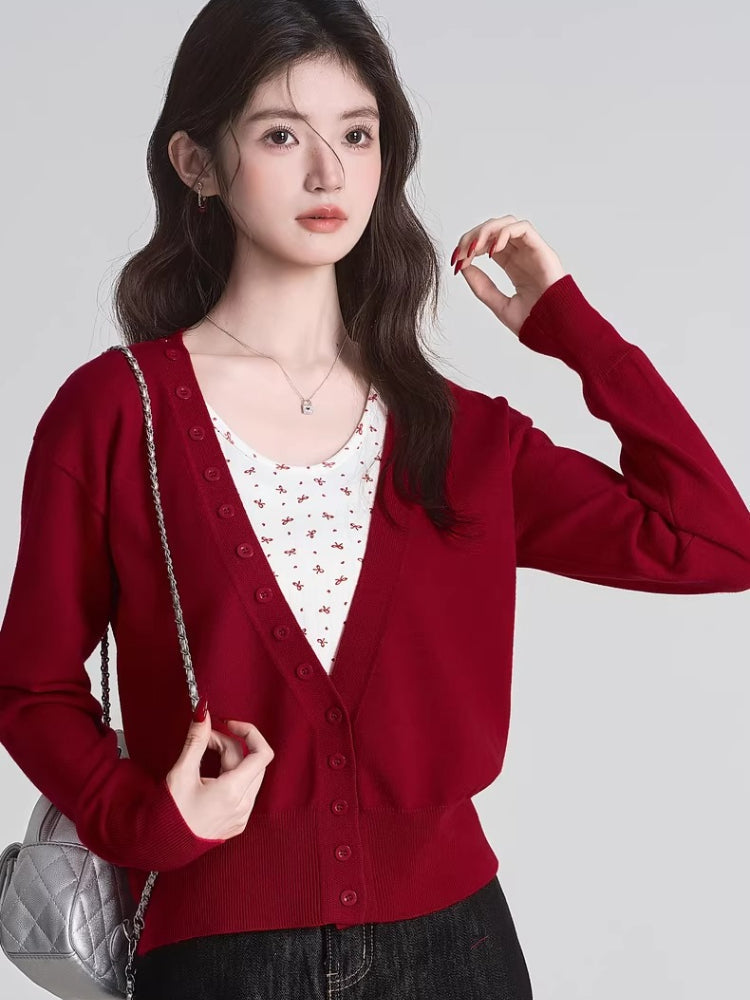 Woman in a red cropped cardigan and floral tank top holding a silver purse.