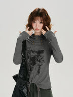 Woman wearing a grey long-sleeve graphic print turtleneck top with thumbhole cuffs and a drawstring hem.