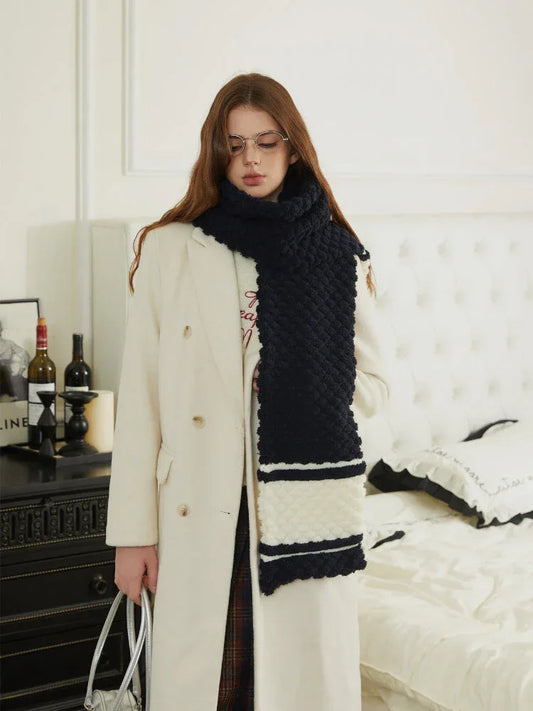 Woman wearing a navy and white striped knit scarf with a cream coat