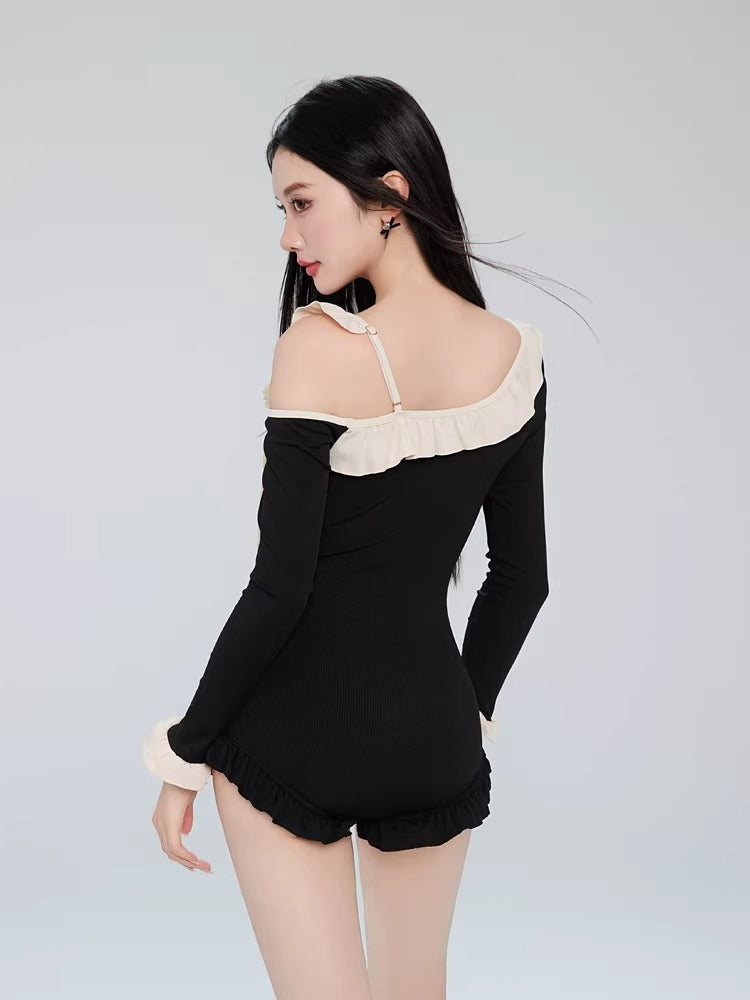 Back view of a woman in a black one-piece swimsuit, showing the off-the-shoulder design and strap detail.