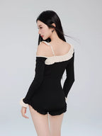 Back view of a woman in a black one-piece swimsuit, showing the off-the-shoulder design and strap detail.