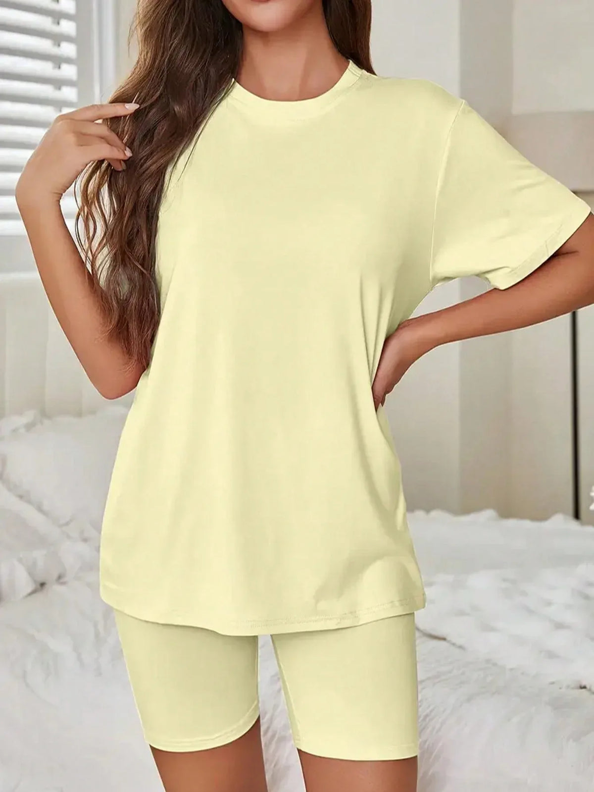 Woman in a light yellow t-shirt and biker shorts set with hands on her hips.