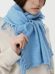 Woman adjusting a light blue fringed scarf.