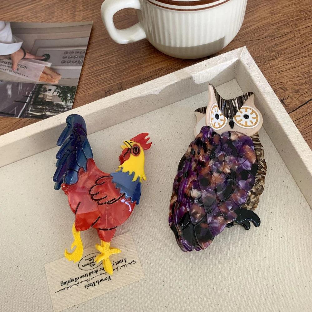 An acrylic rooster hair clip and an acrylic owl hair clip on a white tray