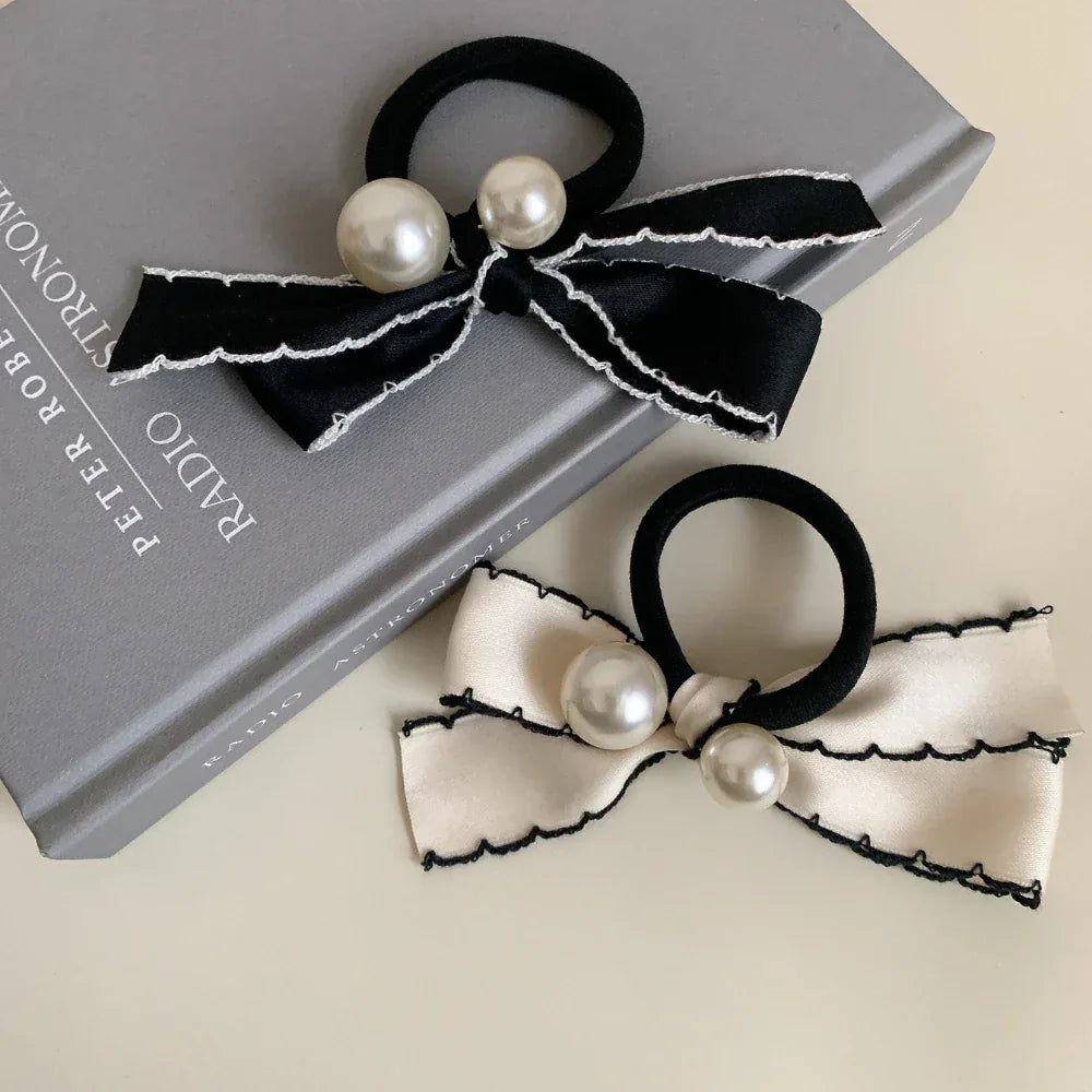 Two bow hair ties, one black and one cream, adorned with pearls and decorative trim, are placed on top of a book.