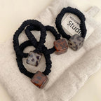 Group of black velvet scrunchies with square leopard print pendants displayed on a textured fabric surface