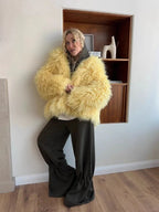 Woman wearing a yellow shaggy faux fur jacket over a light-colored top with dark green pants.