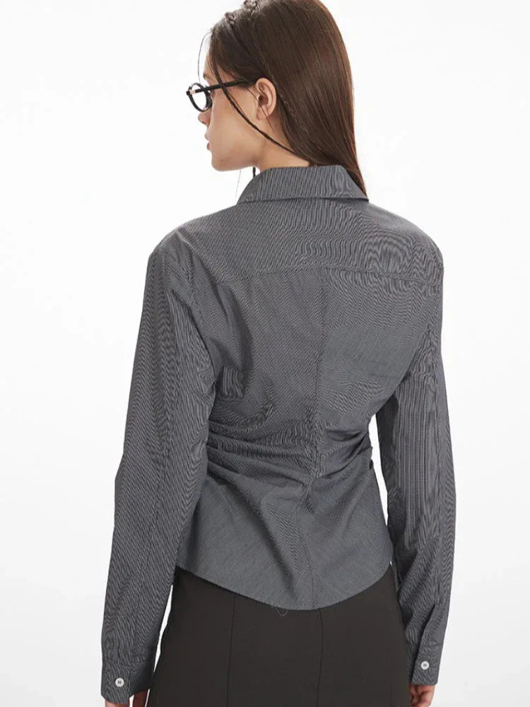 Back view of a woman wearing a grey long-sleeved button-down shirt with ruching detail.