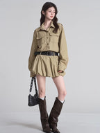 Full body shot of a model in a tan shirt dress with a gathered skirt, black belt, and knee-high boots.