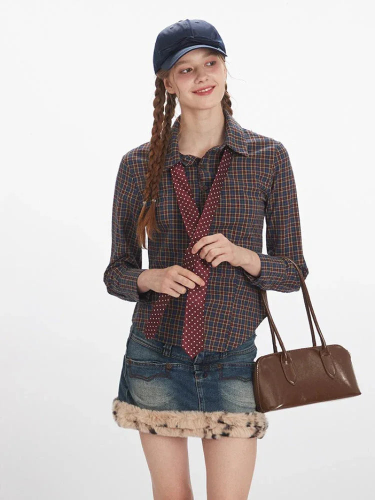 Front view of a woman holding a tie to her chest, wearing a plaid button-down shirt, denim mini skirt with faux fur trim, and a handbag.